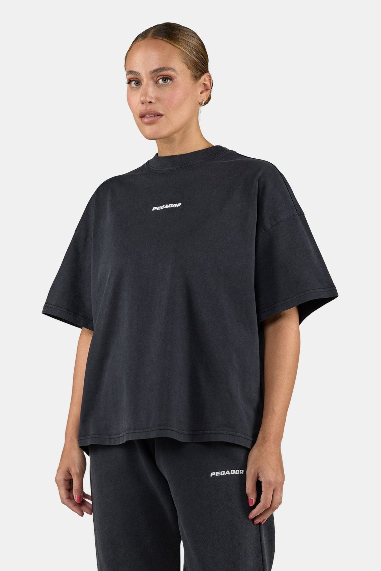 Person wearing a black oversized t-shirt with a brand logo on a plain background